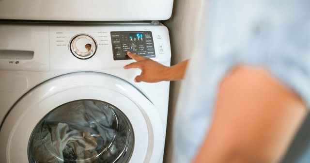 Een hand kiest een programma op het bedieningspaneel van een wasmachine met een volle trommel