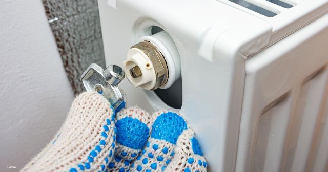 Een hand in een blauw-witte gebreide want zet een sleutel op de aansluiting van een witte radiator