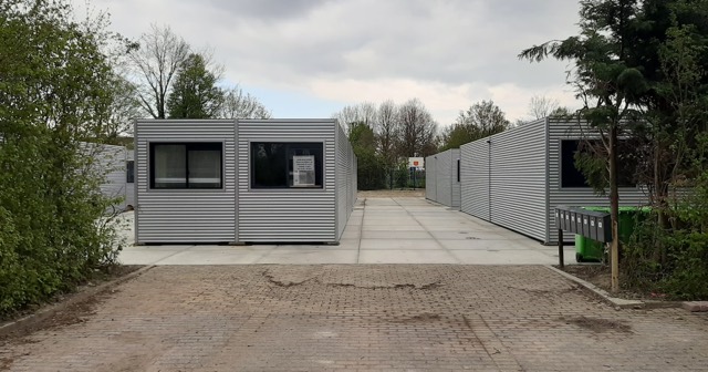 Grijze noodwoningen van geribbeld plaatstaal op het voormalige tennisterrein in Nisse