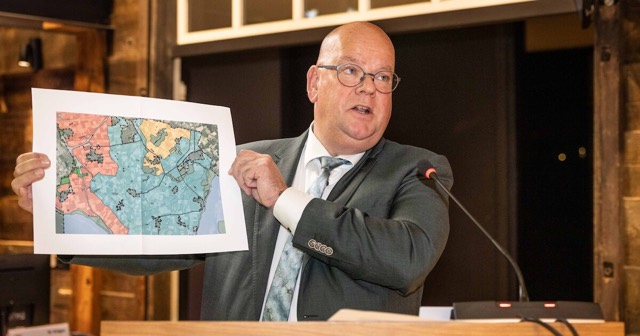 Een wethouder houdt achter de katheder in de raadzaal een gekleurde bestemmingskaart omhoog
