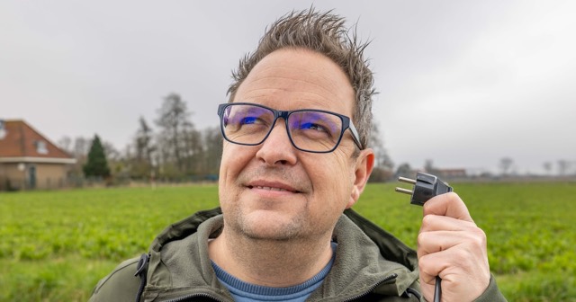 Theo van der Sluijs houdt een stekker omhoog in een weiland bij een boerderij