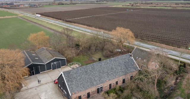 Luchtfoto van een negentiende-eeuwse boerderij met schuren, met daarachter een boomgaard en akkers