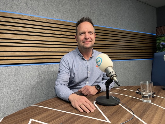 Theo van der Sluijs zit aan tafel achter een microfoon in de radiostudio
