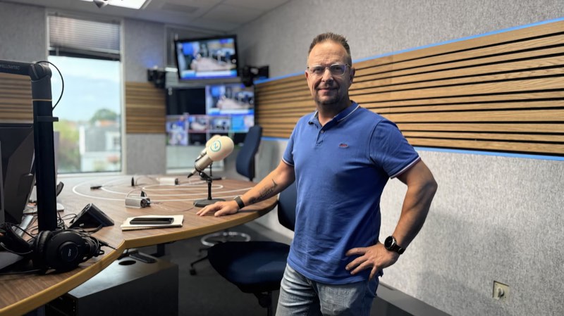 Theo van der Sluijs staat in de radiostudio van Omroep Zeeland, met een hand op de tafel naast de microfoon